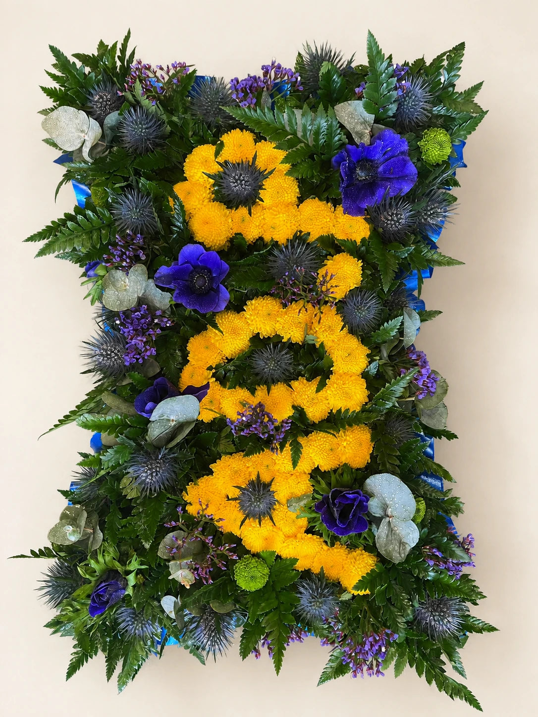 Green foliage funeral pillow with yellow floral DAD lettering and blue and purple flowers