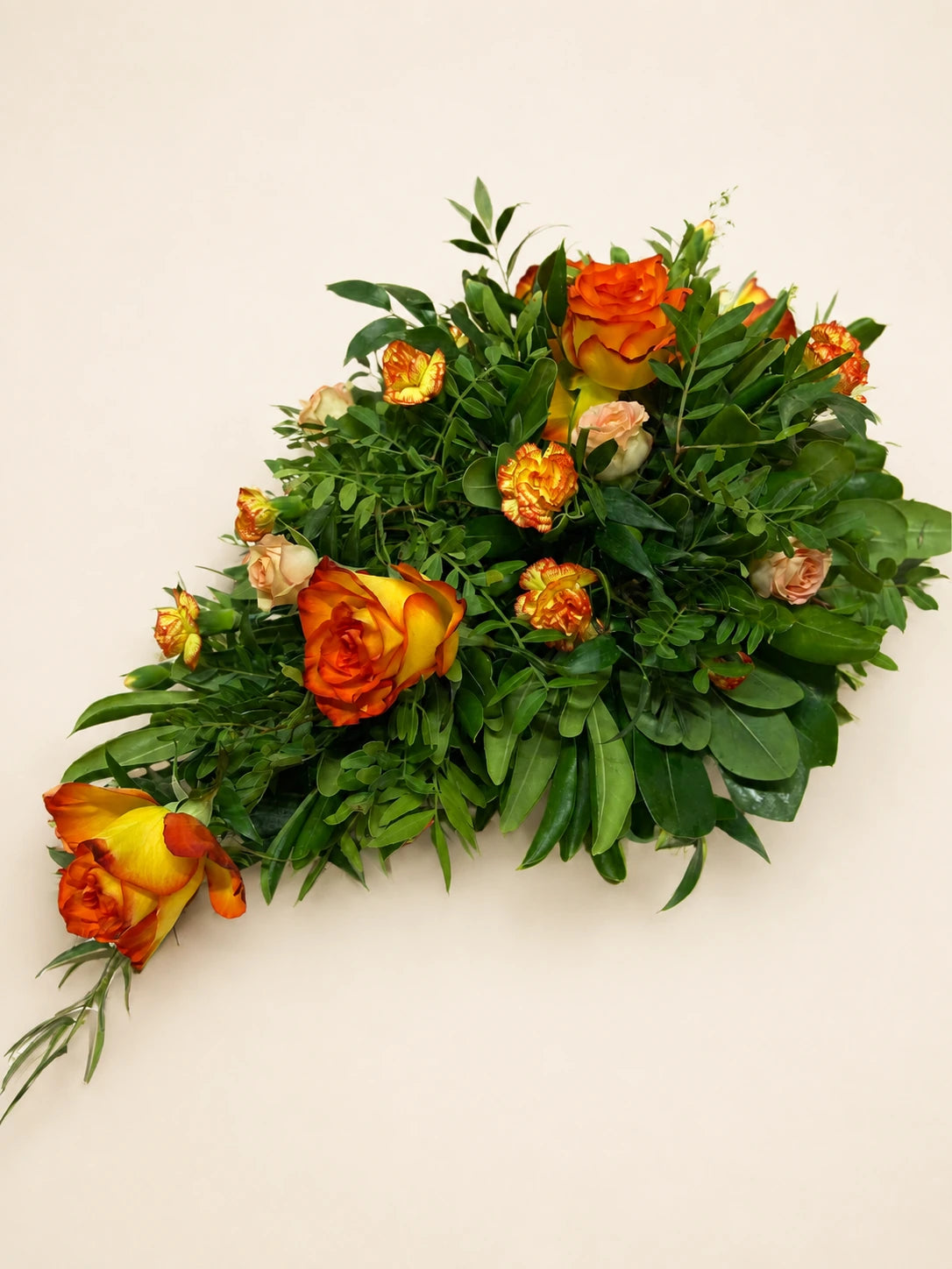 Single-ended funeral spray with orange roses, small orange flowers and layered green foliage