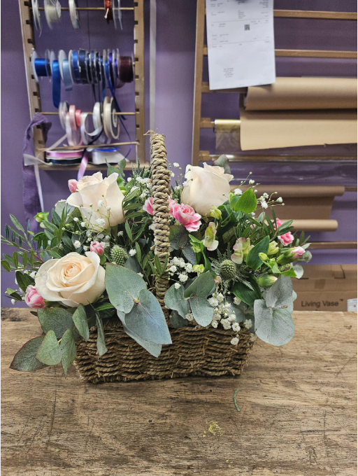 Pastel flower basket with blush roses, eucalyptus and white blooms on a shop counter