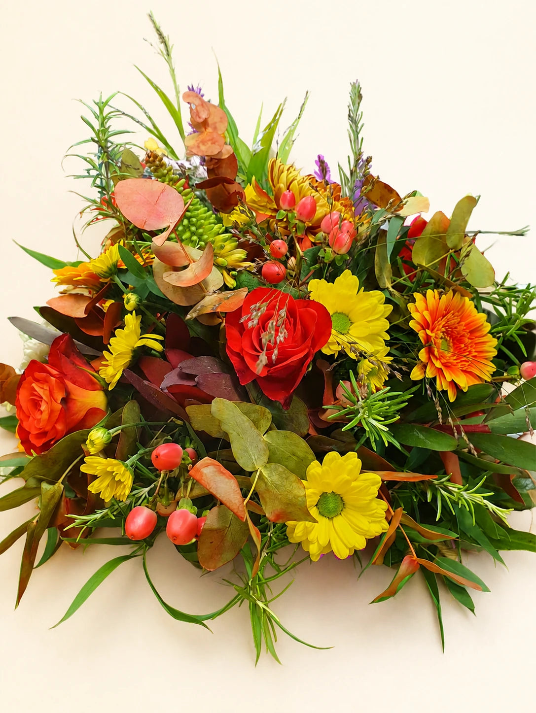 Autumnal funeral posy with orange roses, yellow and orange flowers, berries and mixed foliage