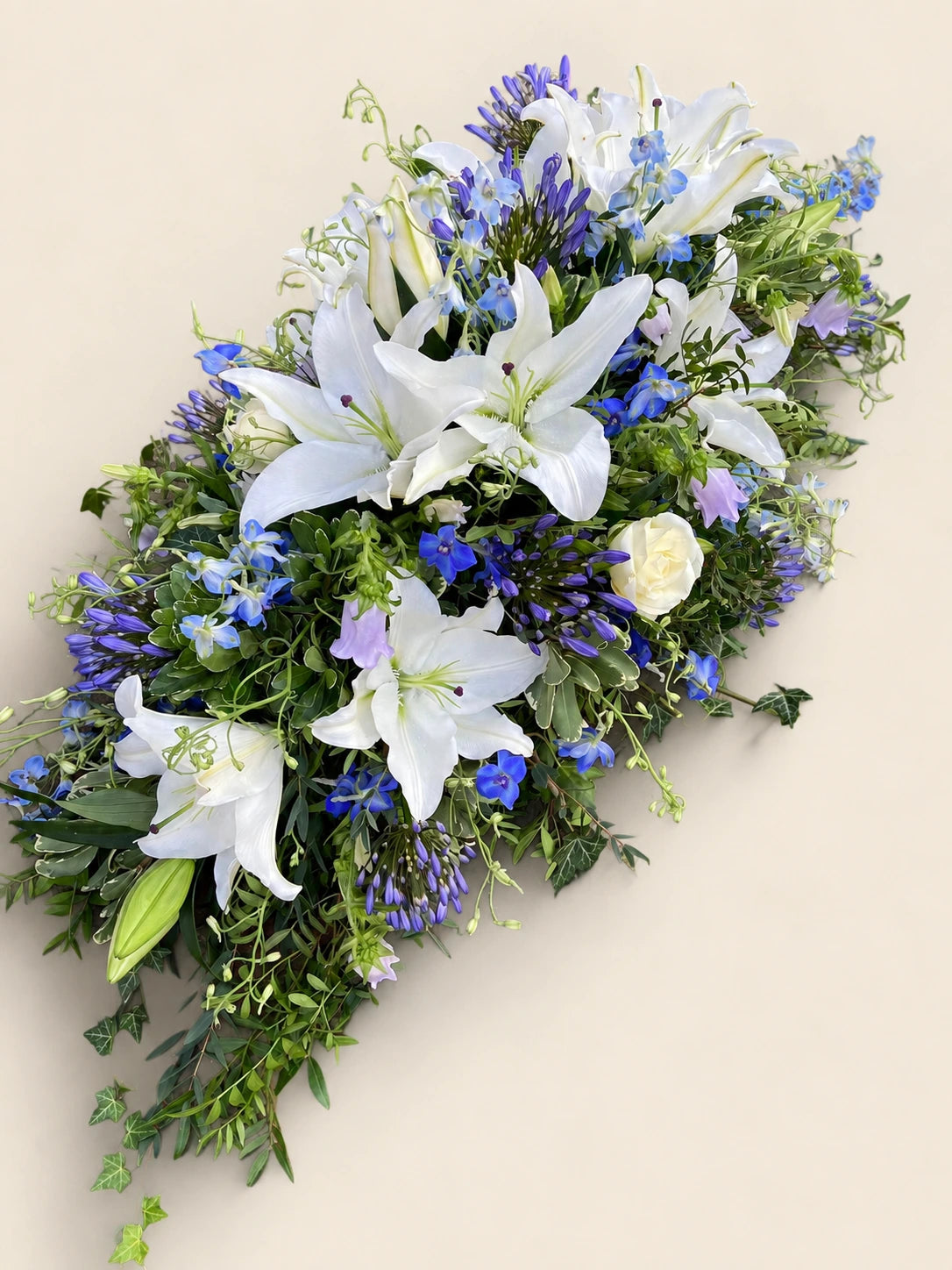 Blue and white lily funeral casket spray with agapanthus and trailing greenery