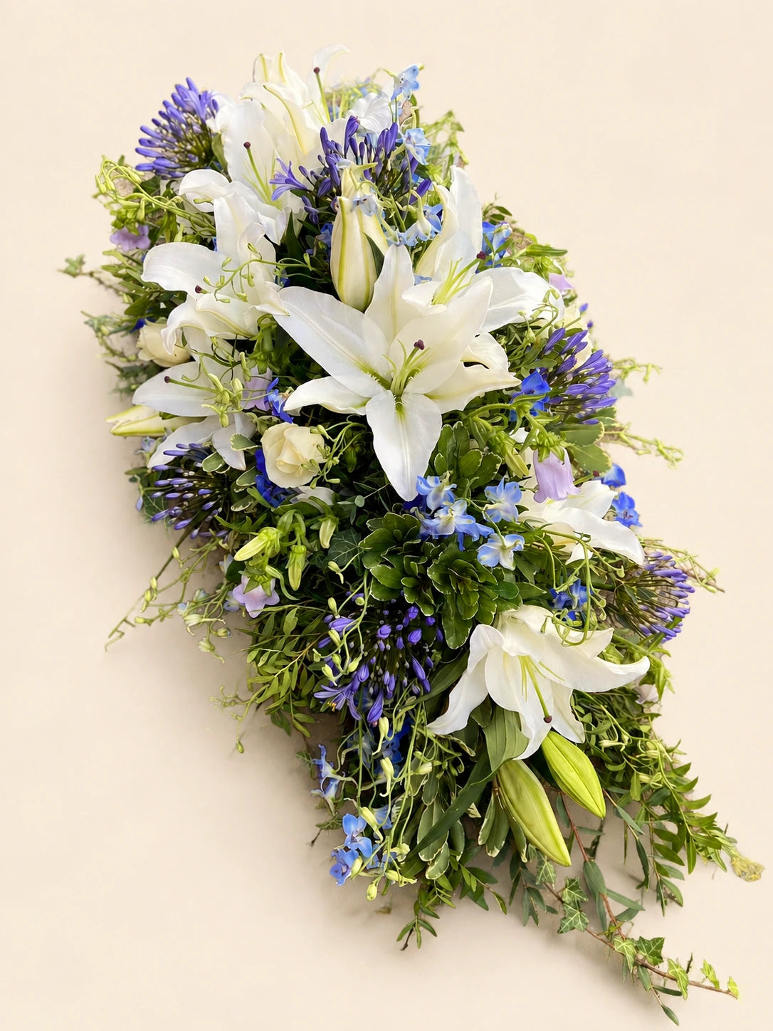 White lily and blue agapanthus funeral casket spray from the opposite side