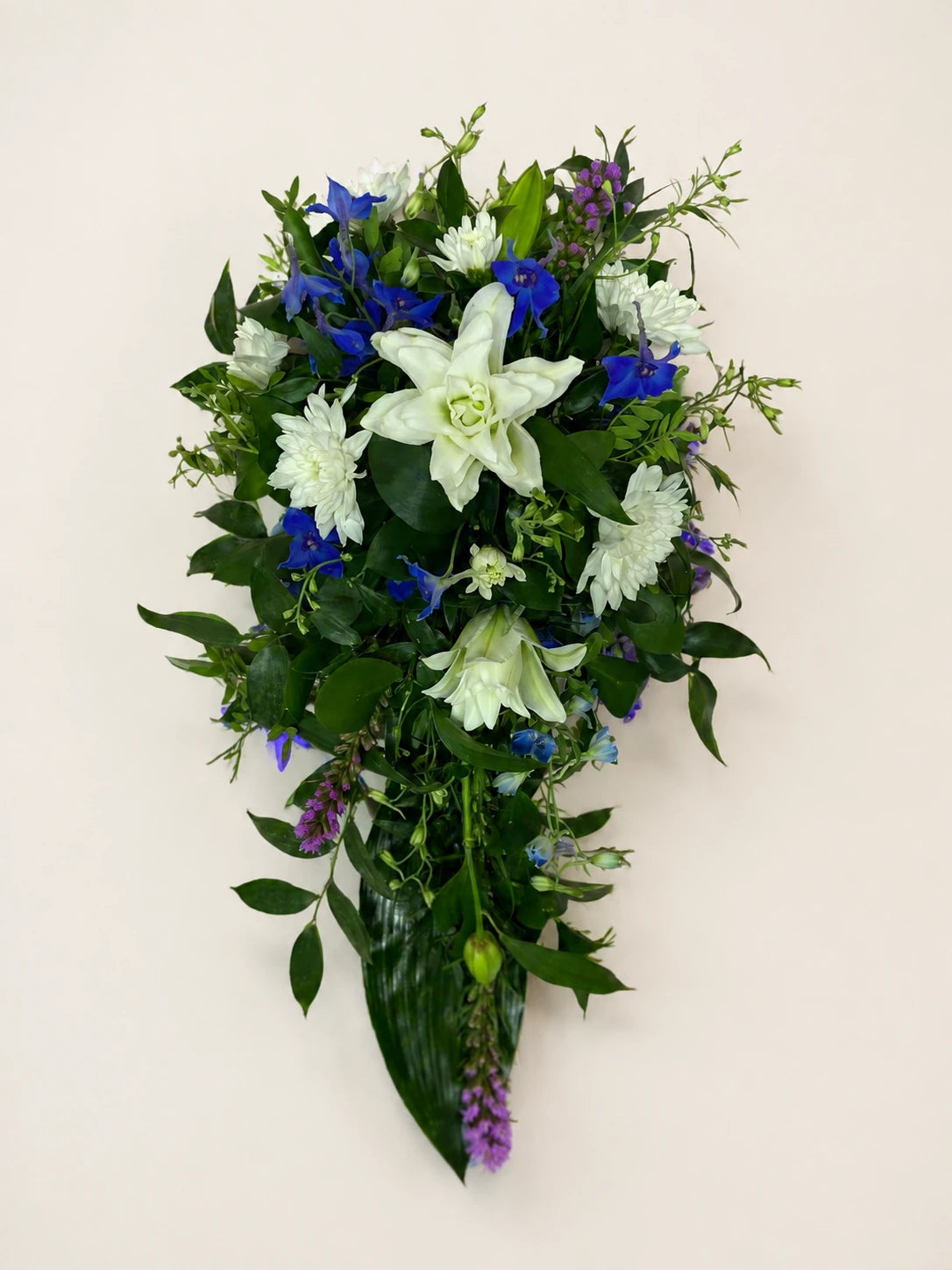 Blue and white single-ended funeral spray with a white lily, blue flowers and green foliage