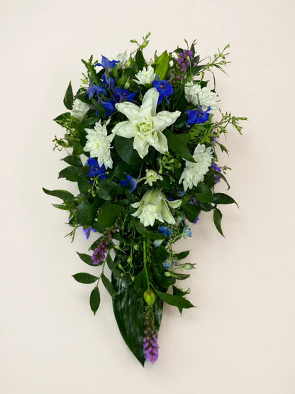 Blue and white single-ended funeral spray with a white lily, blue flowers and green foliage
