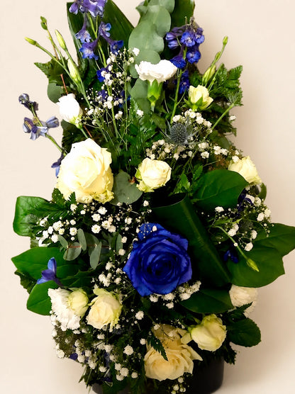 Close view of a blue and white funeral spray with a blue rose, cream roses and gypsophila