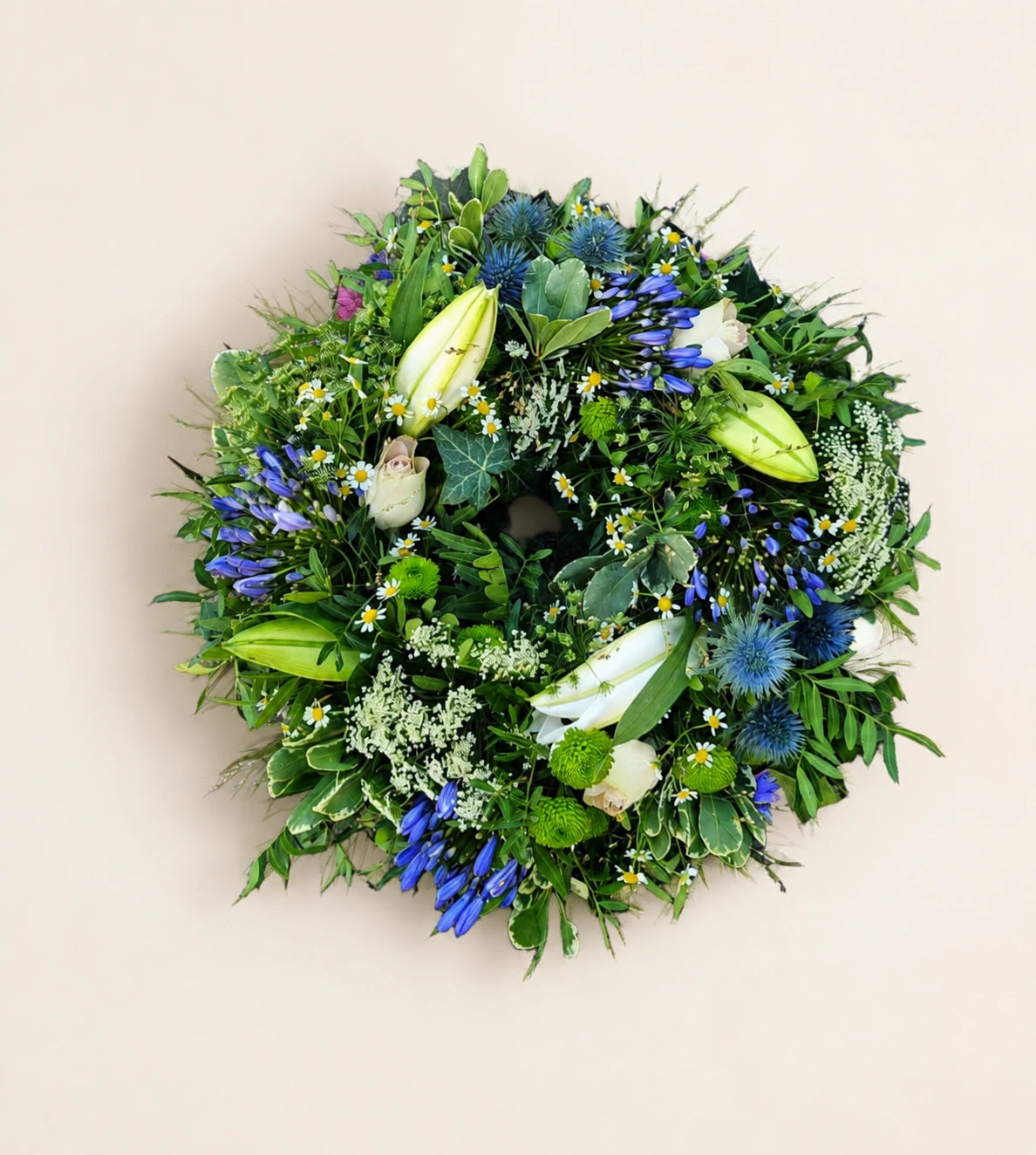 Circular funeral wreath with blue flowers, white lily buds, thistles and mixed green foliage