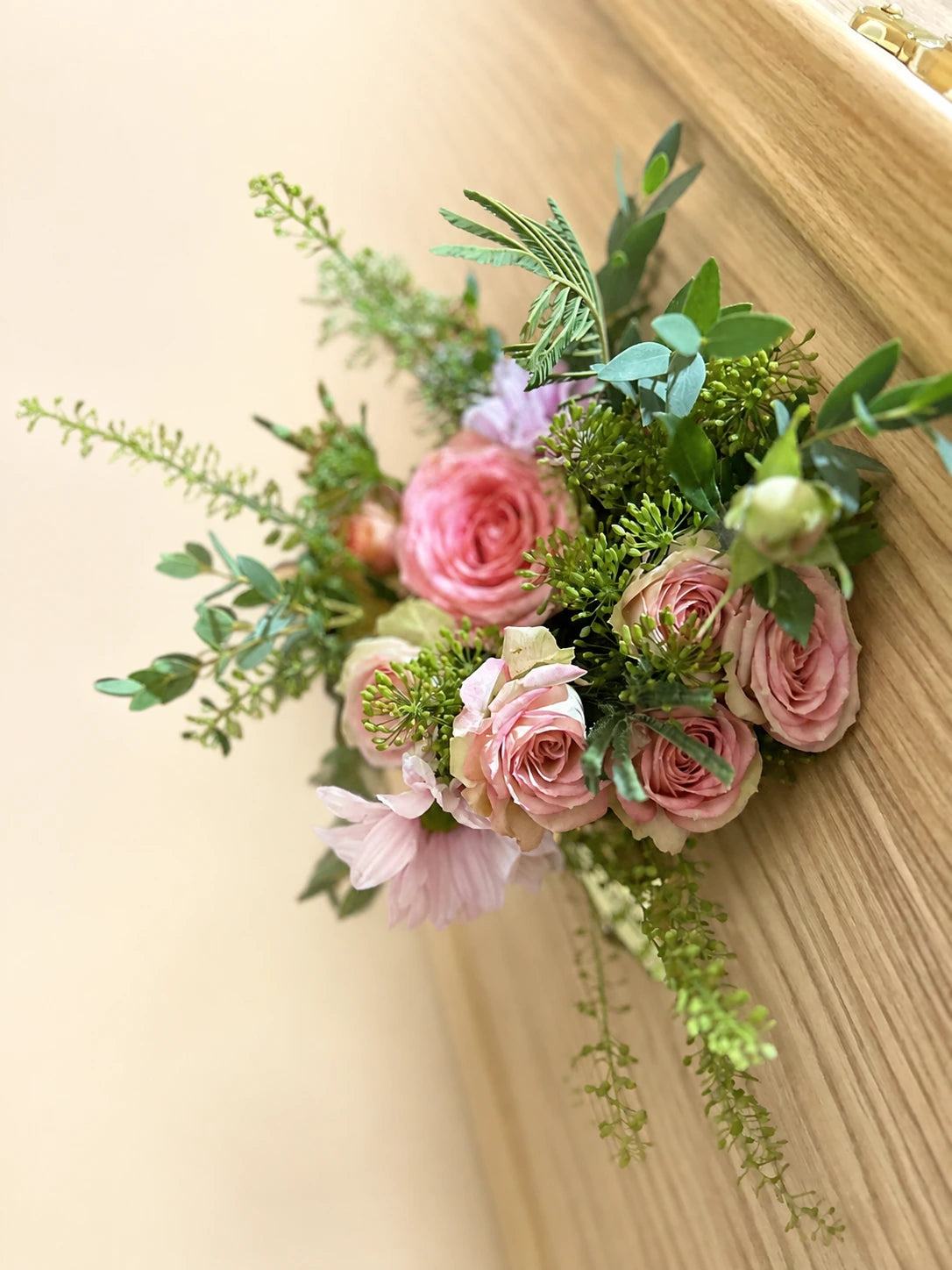 Pink rose and foliage corsage attached to the side of a wooden casket
