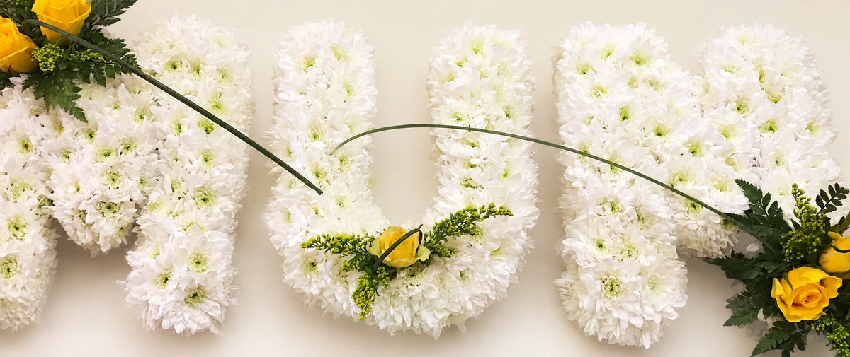 White chrysanthemum letters spelling MUM with yellow flower accents and curved grasses