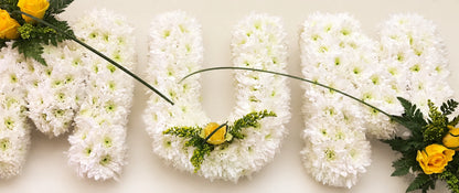 White chrysanthemum letters spelling MUM with yellow flower accents and curved grasses