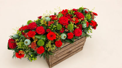 Angled view of a red and green contemporary casket spray on a wooden display crate
