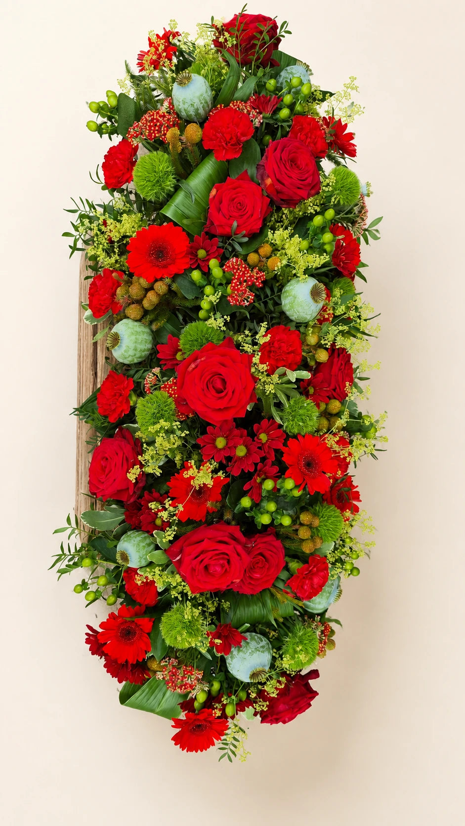 Overhead view of a contemporary funeral casket spray with red flowers and green accents
