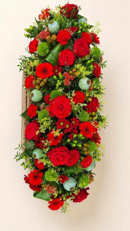 Overhead view of a contemporary funeral casket spray with red flowers and green accents