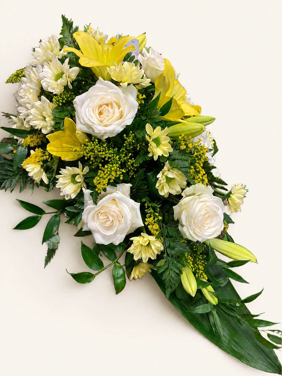 Single-ended funeral spray with cream roses, yellow flowers, lily buds and green foliage