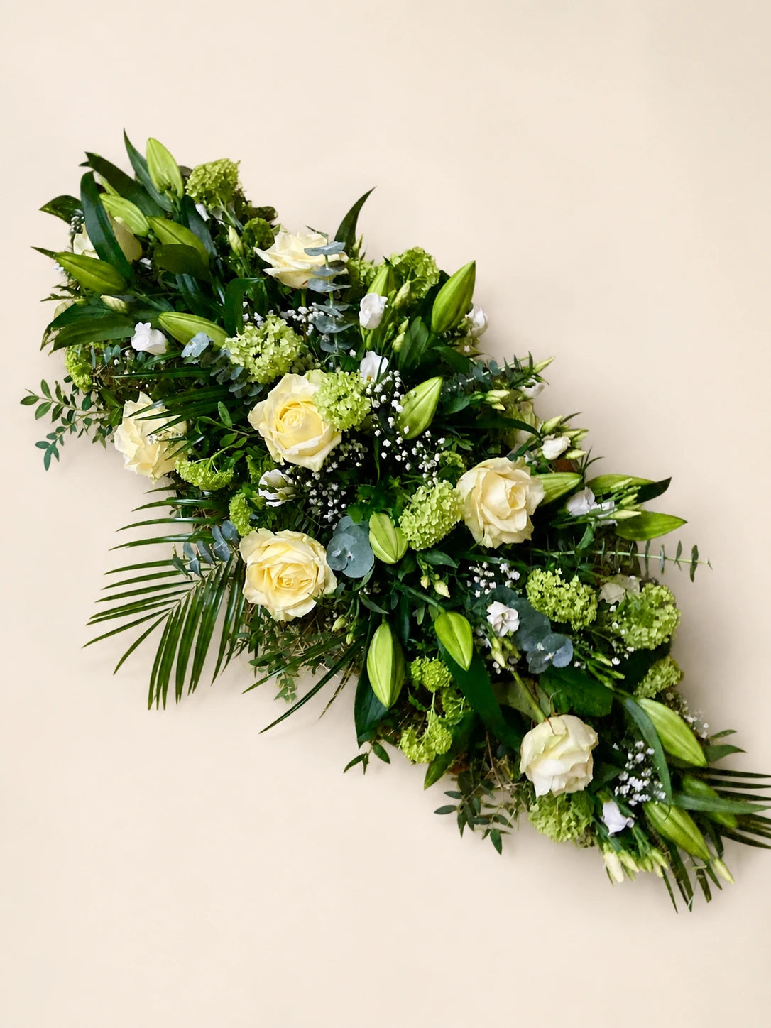 Cream rose and lily funeral casket spray with green viburnum and palm foliage