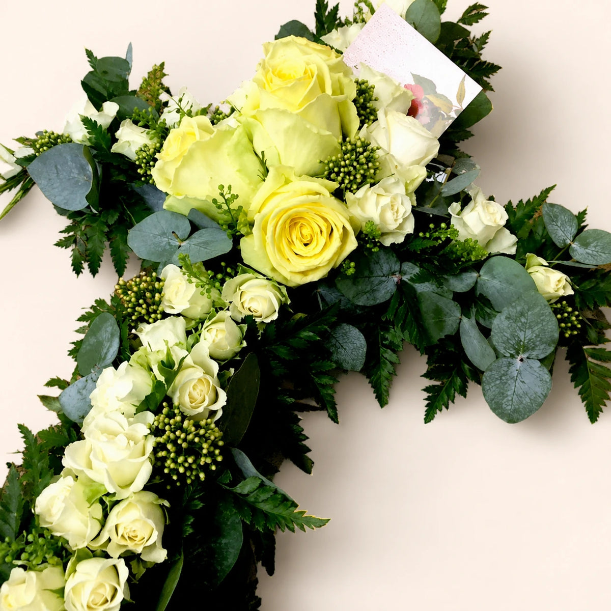 Close view of a funeral cross with pale yellow and cream roses and eucalyptus foliage