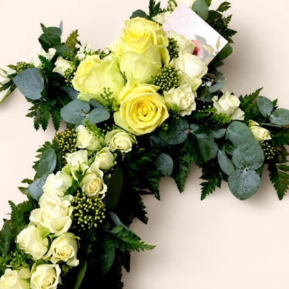 Close view of a funeral cross with pale yellow and cream roses and eucalyptus foliage