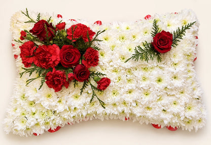 White floral funeral pillow with a red rose corsage and a single red rose accent
