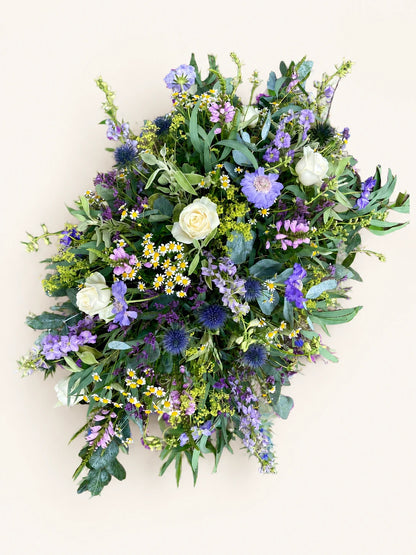 Funeral casket spray with cream roses, lilac and purple flowers and eucalyptus foliage