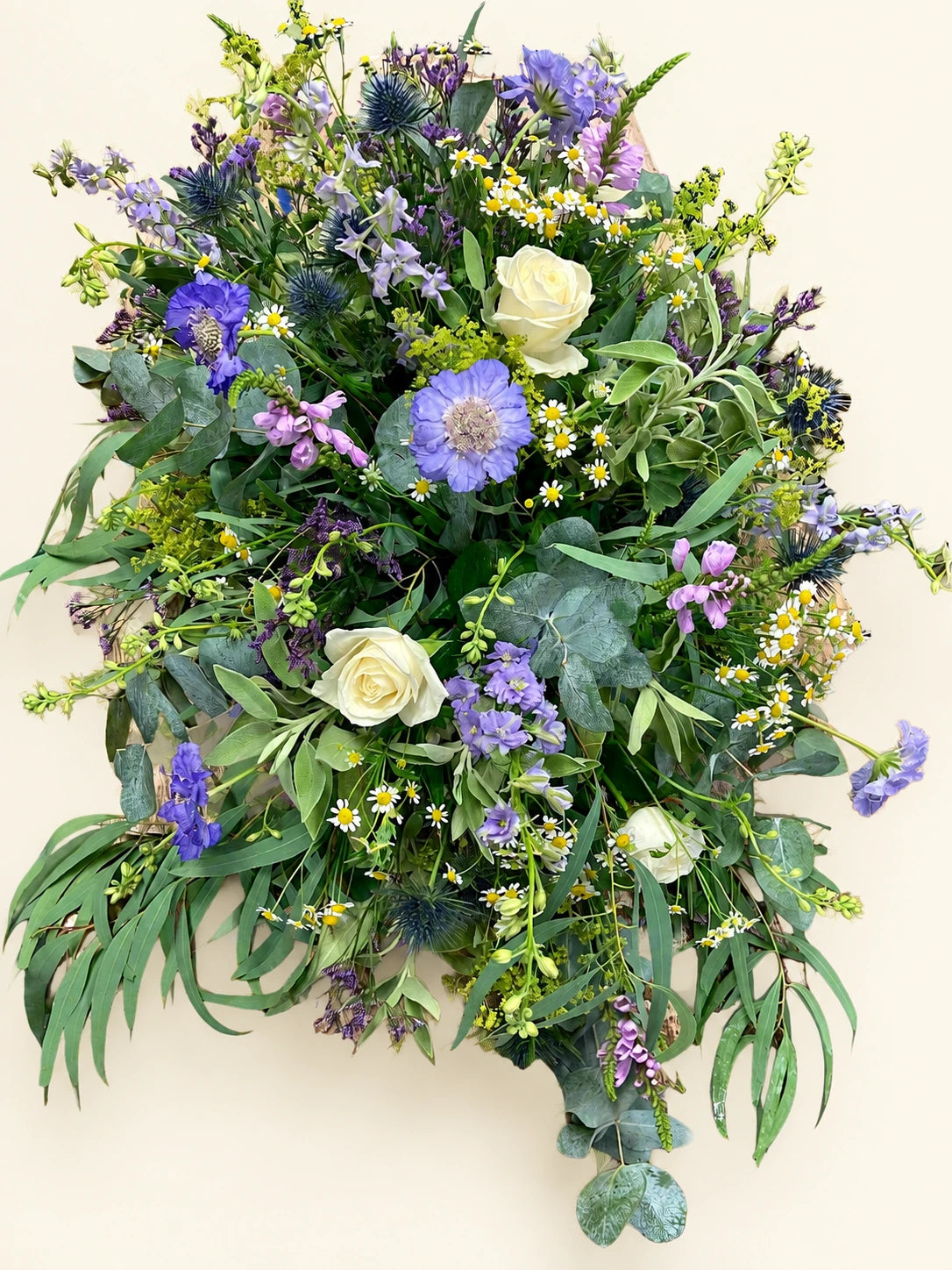 Close view of cream roses and lilac flowers among eucalyptus in a funeral casket spray
