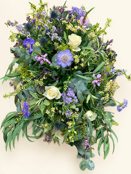 Close view of cream roses and lilac flowers among eucalyptus in a funeral casket spray