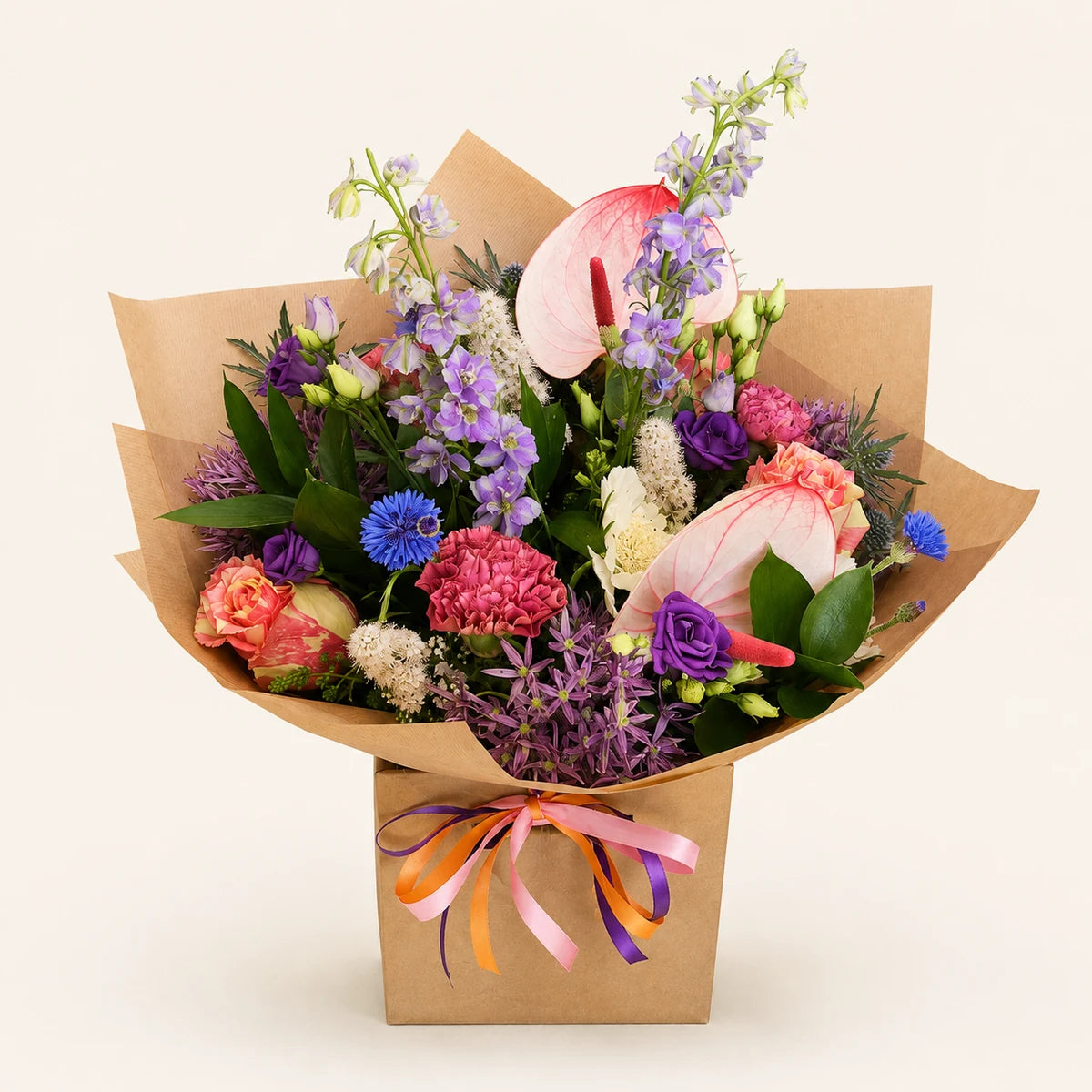 A vibrant mixed flower bouquet wrapped in brown kraft paper and tied with a pink, orange, and purple ribbon, set against a solid light beige background.