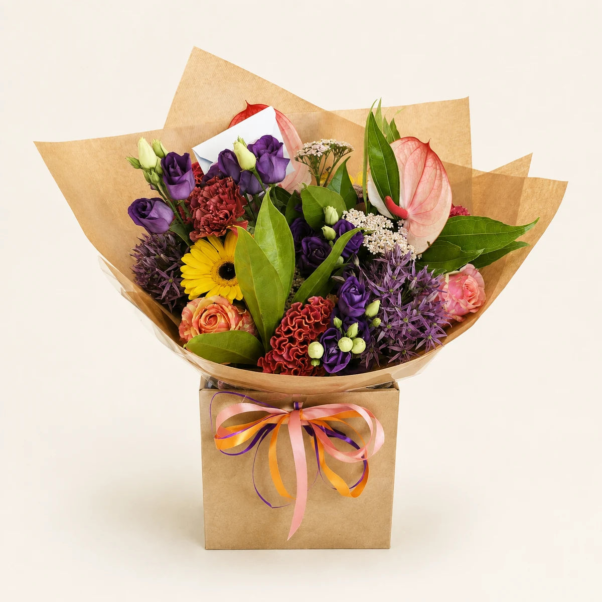 A vibrant mixed flower bouquet in a square kraft paper box, wrapped in brown paper with a pink and orange striped ribbon. The bouquet features a variety of colorful flowers including purple hydrangeas, a yellow sunflower, pink anthurium, and green foliage, set against a clean, light beige background.