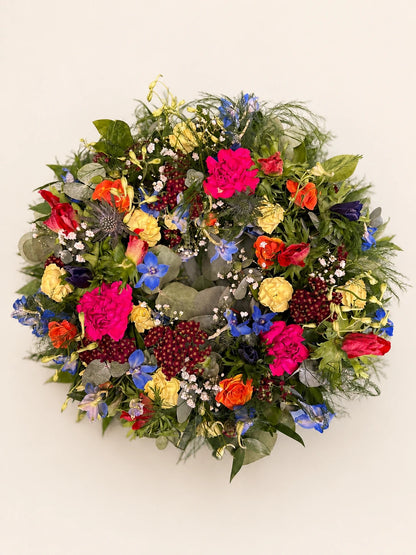 Overhead view of a mixed funeral wreath with orange roses, bright pink flowers, berries and foliage