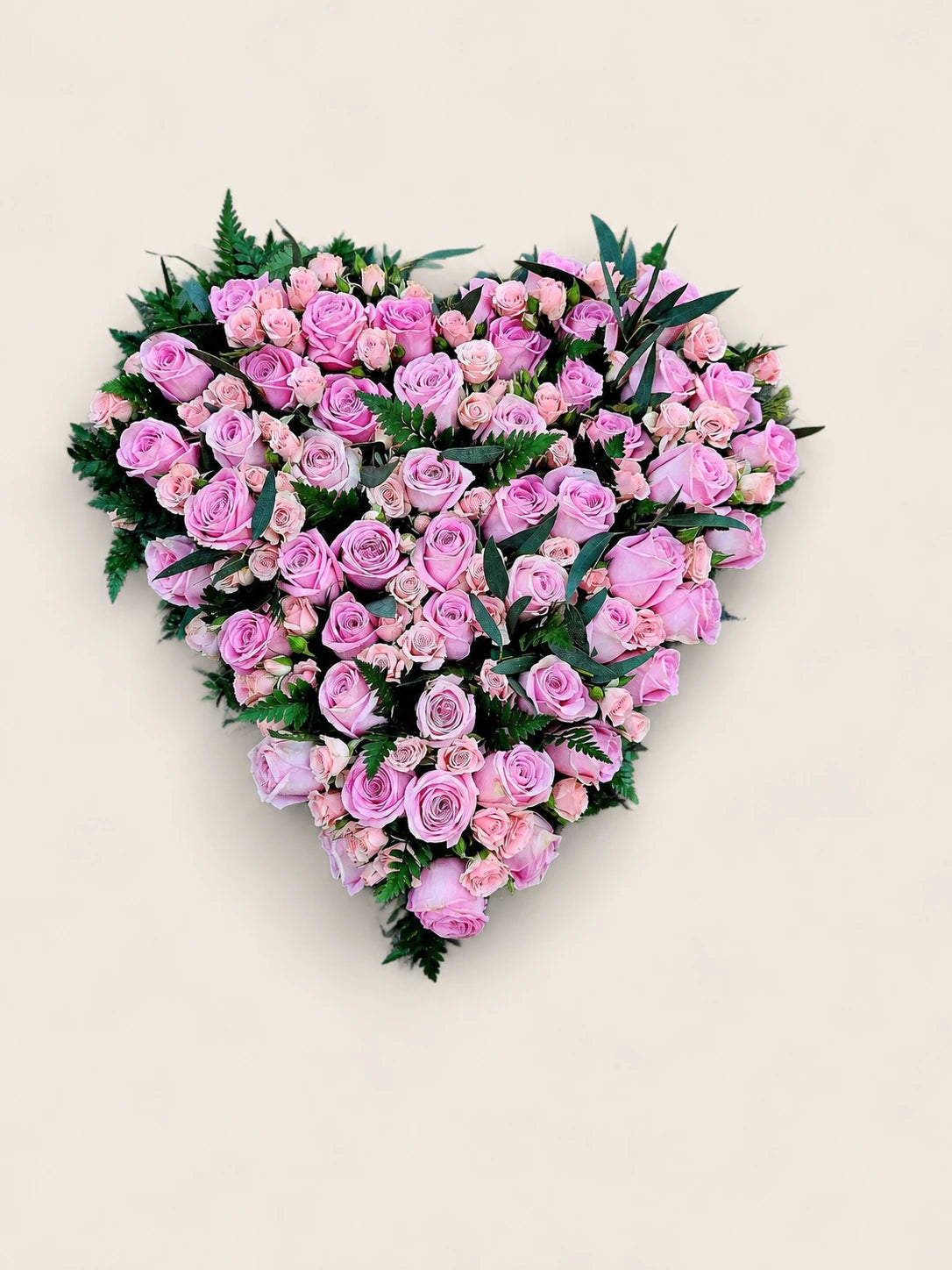 Heart-shaped funeral tribute filled with pale pink roses and edged with green foliage