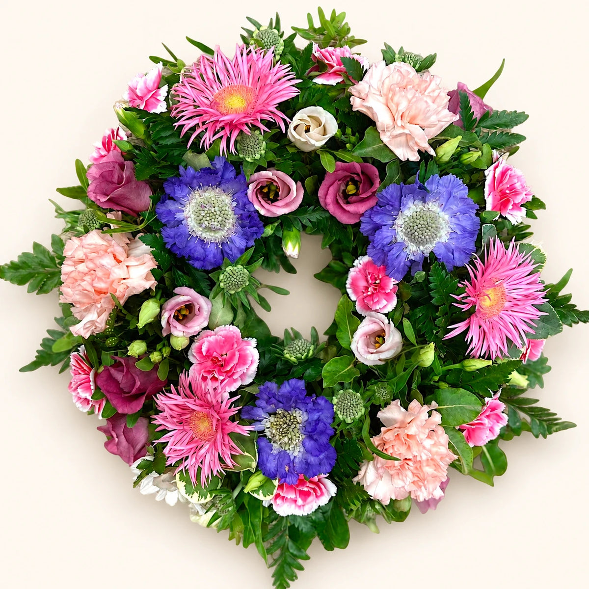 Funeral wreath with pink gerberas and carnations, purple flowers and green foliage