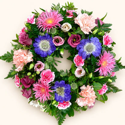 Funeral wreath with pink gerberas and carnations, purple flowers and green foliage