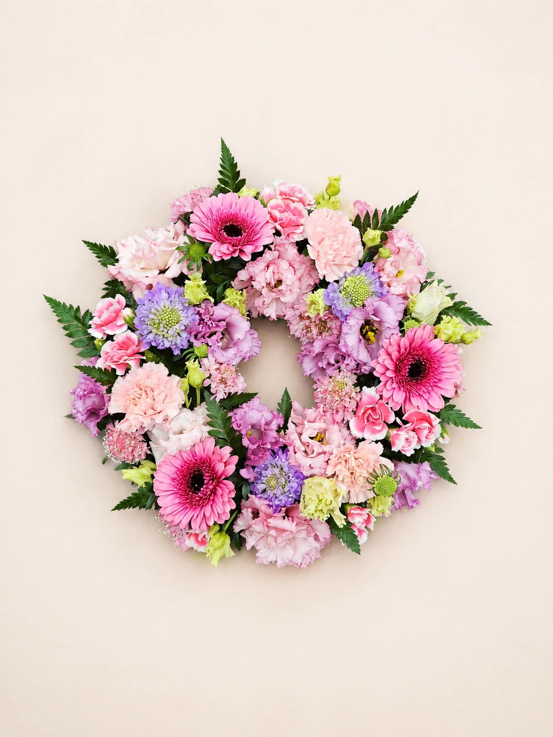 Overhead view of a pink funeral wreath with gerberas, carnations, lilac flowers and pale green accents