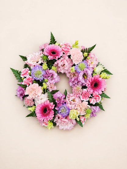 Overhead view of a pink funeral wreath with gerberas, carnations, lilac flowers and pale green accents