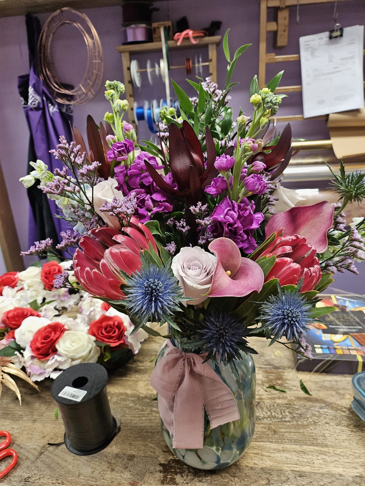 Pink, purple and red vase arrangement with protea, calla lilies and eryngium in a ceramic vase