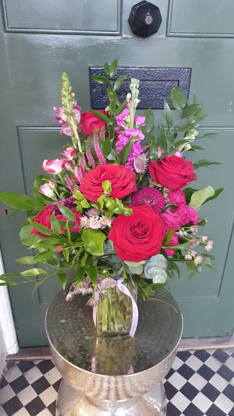 Tall red and pink vase arrangement with roses, snapdragons, veronica and eucalyptus in clear glass