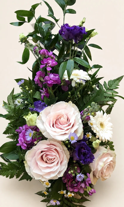Close view of pale pink roses, purple flowers and white daisies in a funeral spray