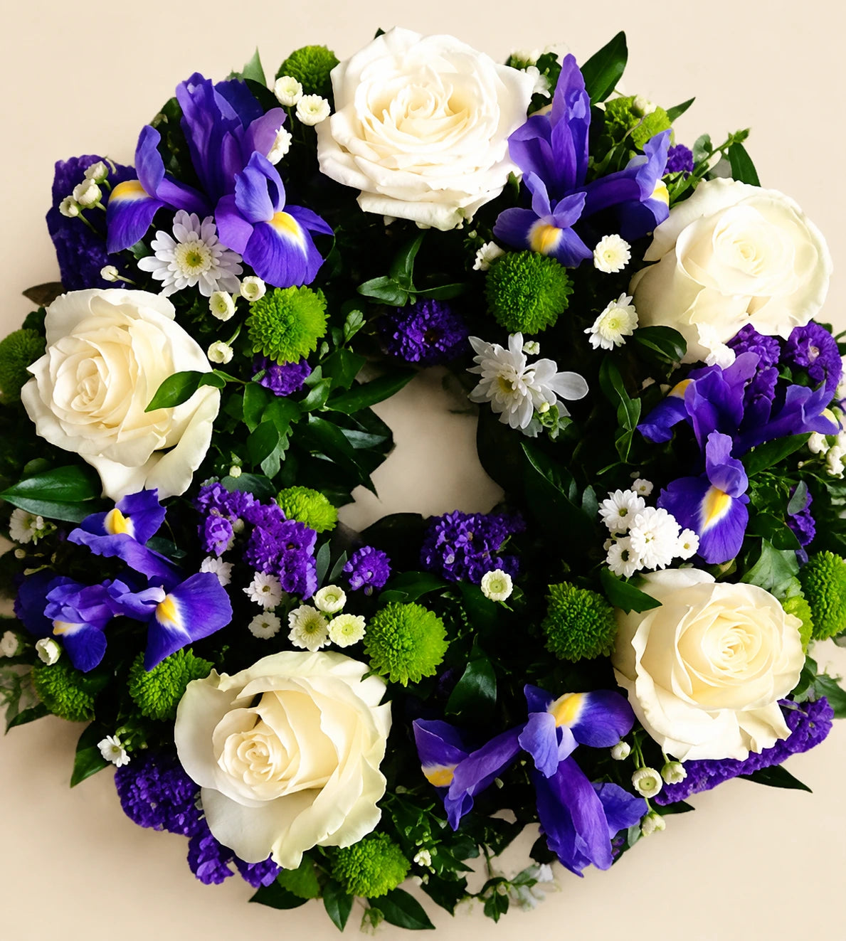 Funeral wreath with cream roses, purple irises, small white flowers and green accents