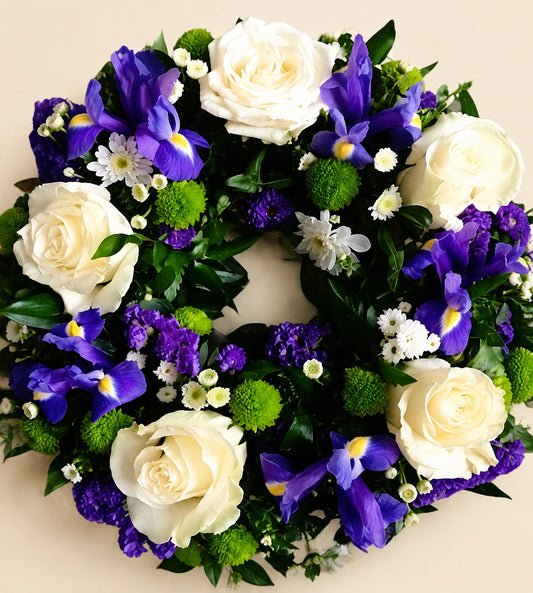 Funeral wreath with cream roses, purple irises, small white flowers and green accents