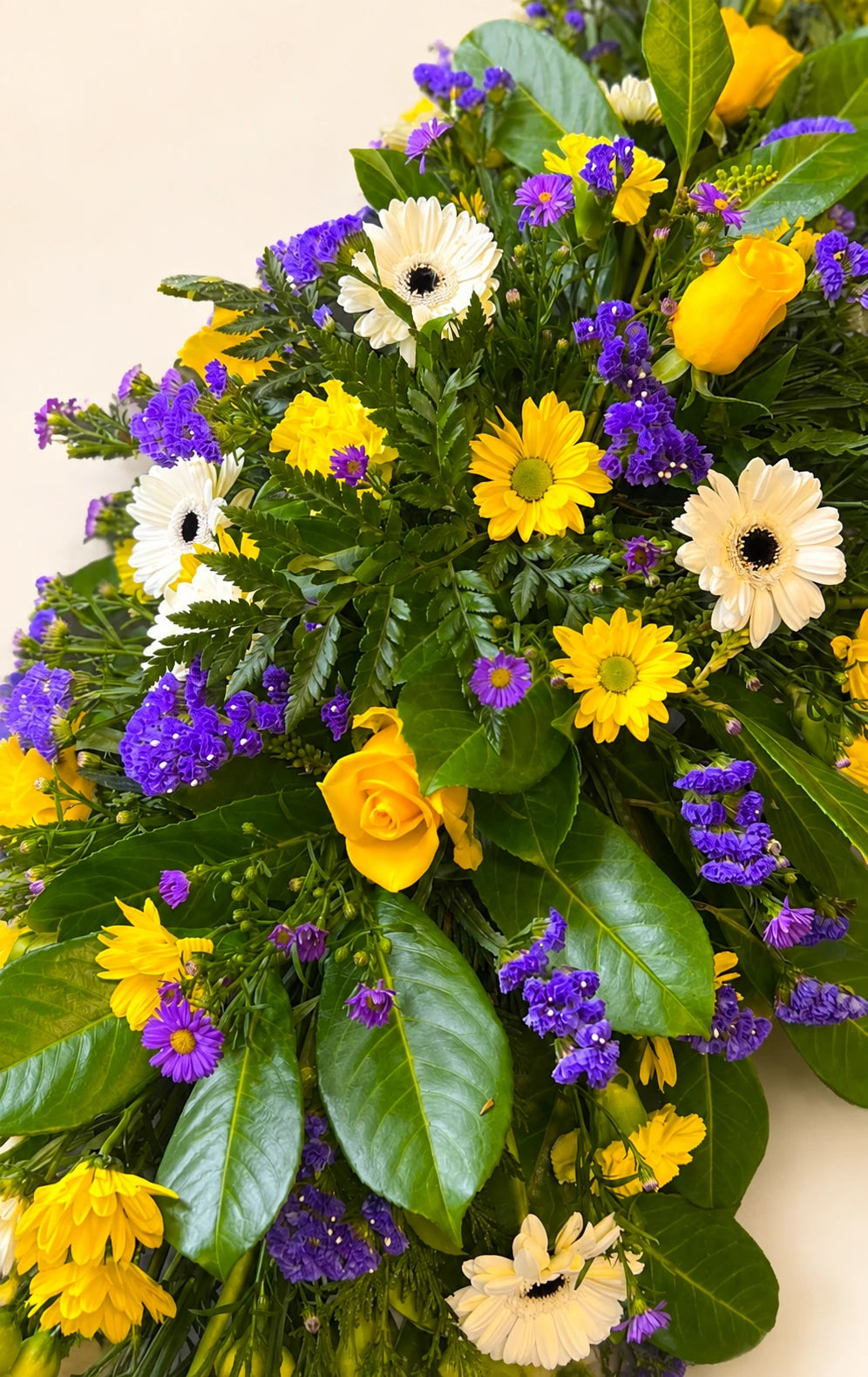 Close view of yellow roses, white gerberas and purple flowers in a funeral spray