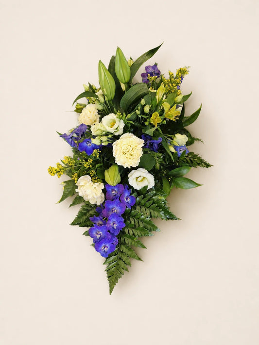 Single-ended funeral spray with purple flowers, pale yellow roses, cream flowers and lily buds