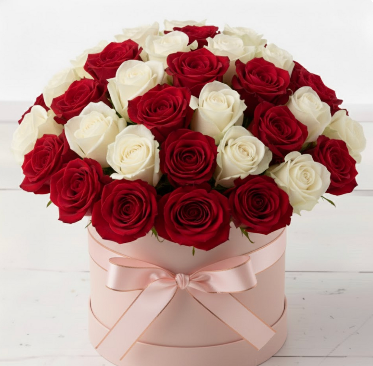 Box of red and white roses with a pink ribbon on a light wooden background