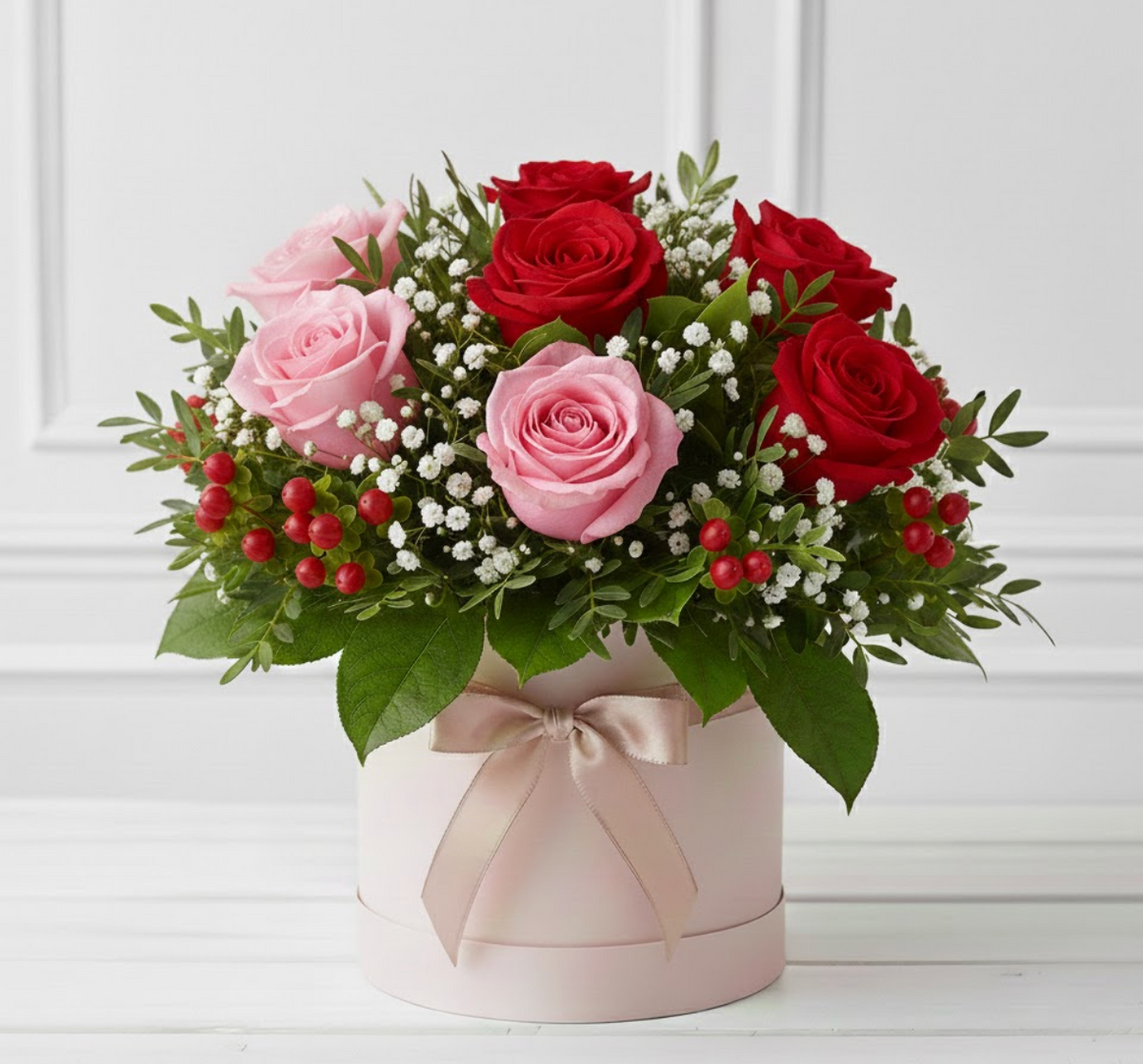 Bouquet of red and pink roses with greenery in a decorative box on a white background