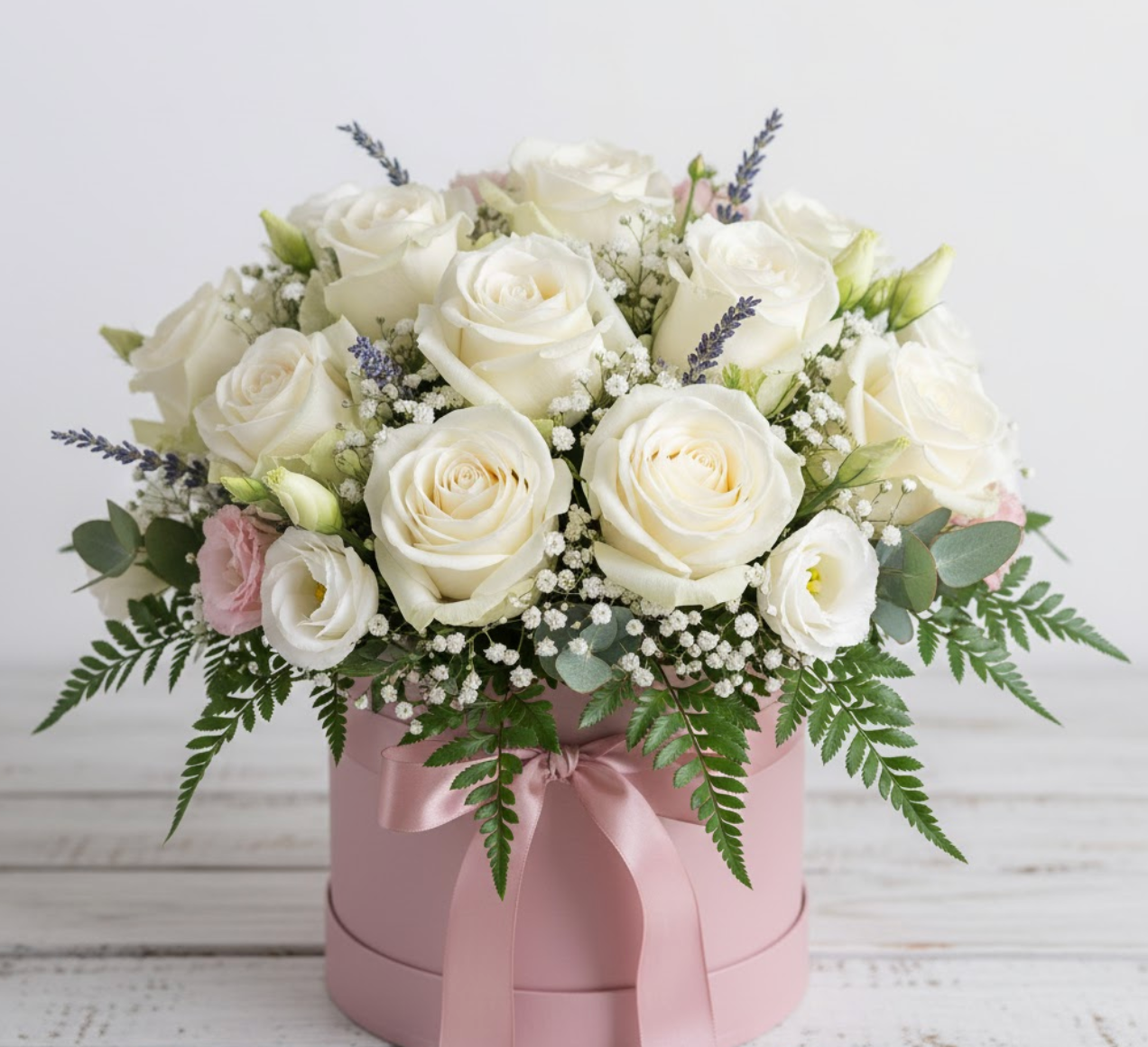 Bouquet of white roses and greenery in a pink hatbox on a light wooden surface.