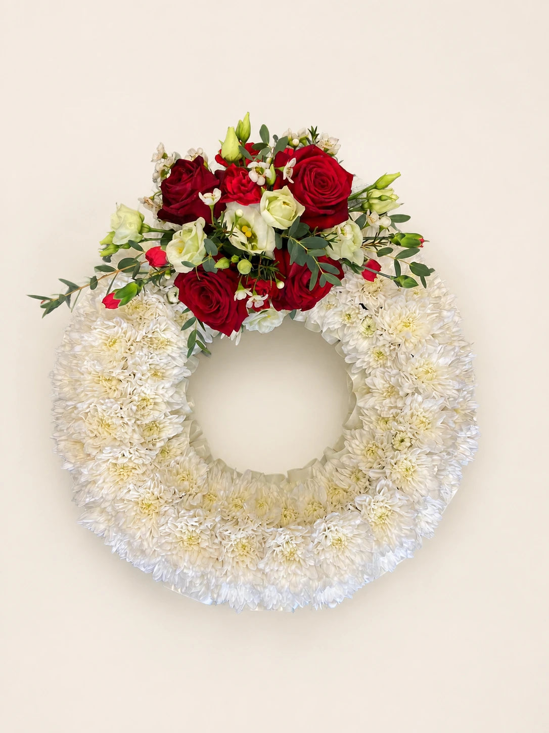 White floral funeral wreath with a top corsage of red and cream roses and green foliage