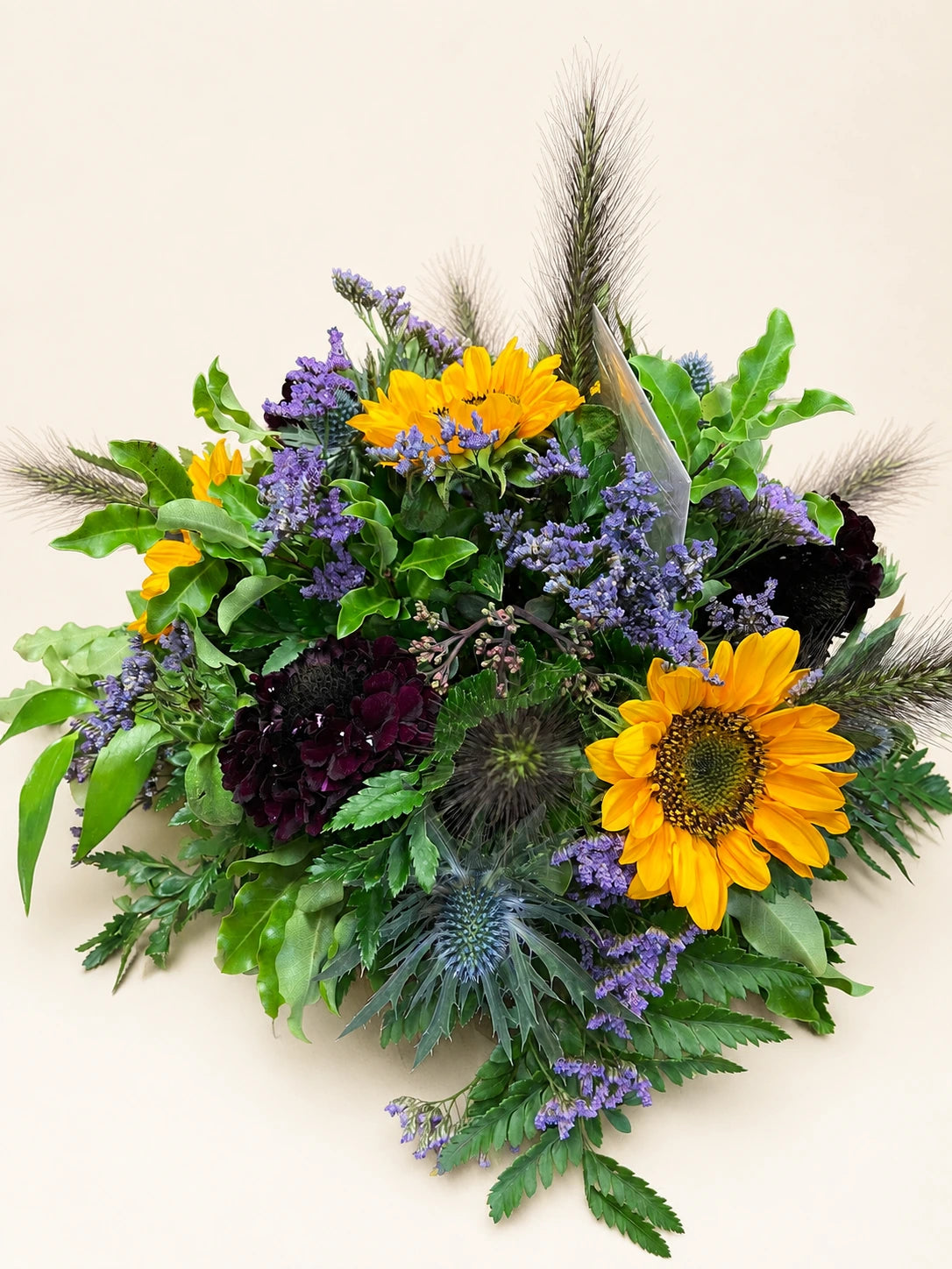 Funeral posy with yellow sunflowers, purple flowers, dark blooms and feathery green foliage