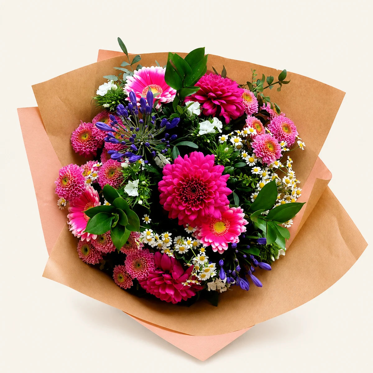 A vibrant mixed flower bouquet featuring bright pink and magenta daisies, deep pink dahlias, purple bellflowers, and small white daisies, wrapped in brown kraft paper and a peach-colored paper sleeve, set against a solid off-white background.