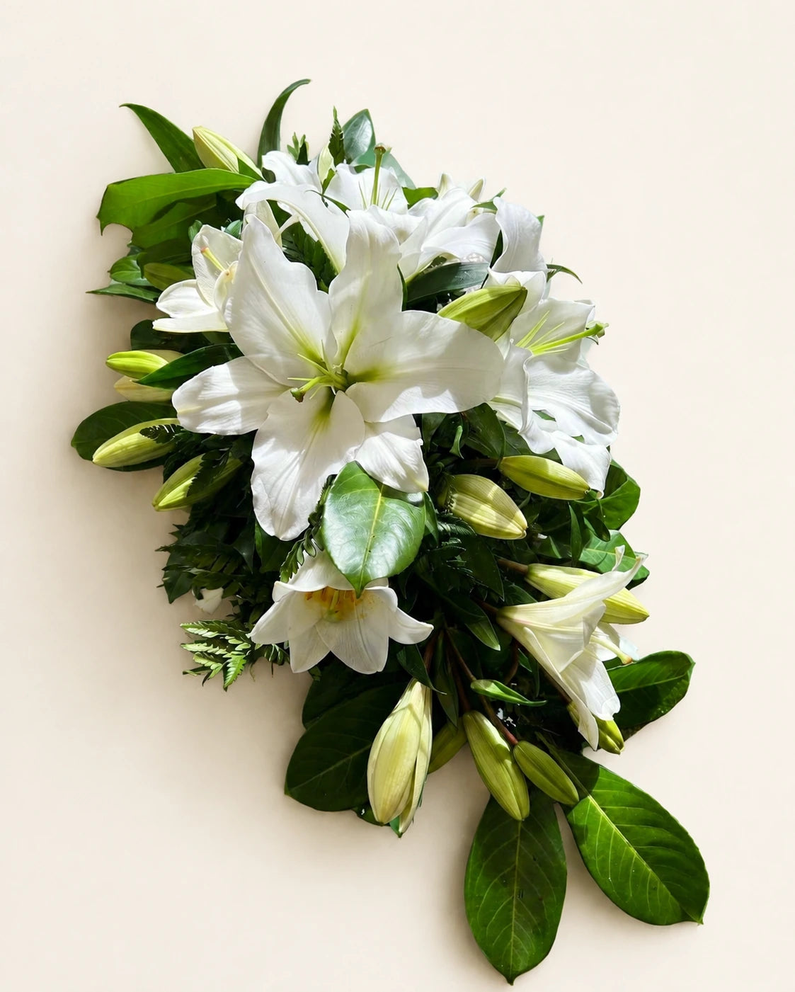 Traditional funeral casket spray with open white lilies, lily buds and glossy green foliage