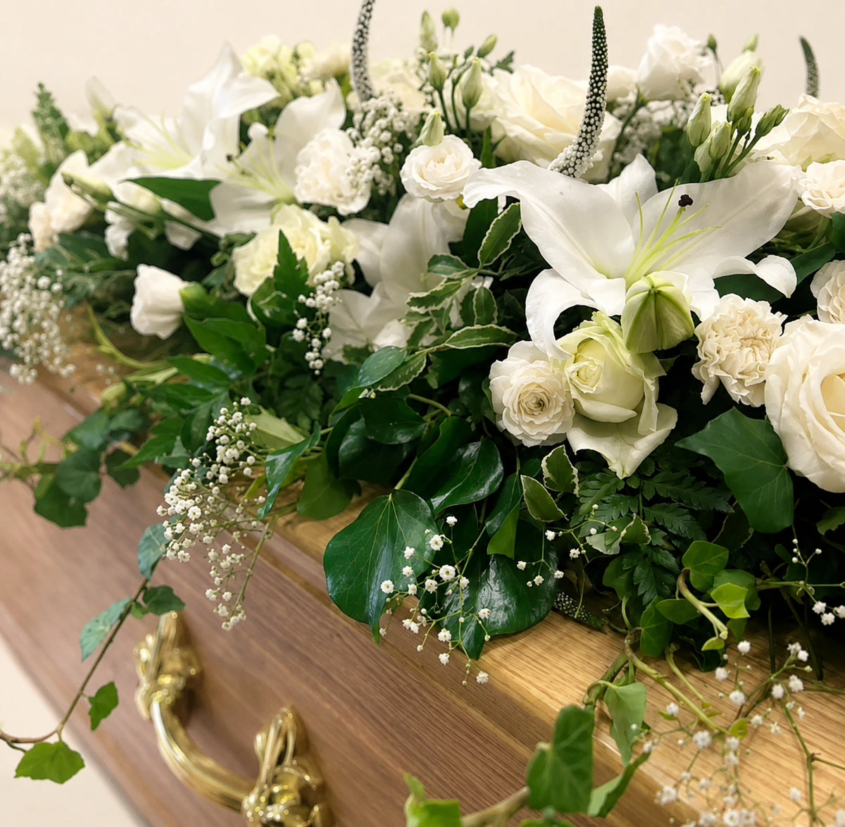 Close view of white lilies, roses and gypsophila in a casket spray on a wooden coffin