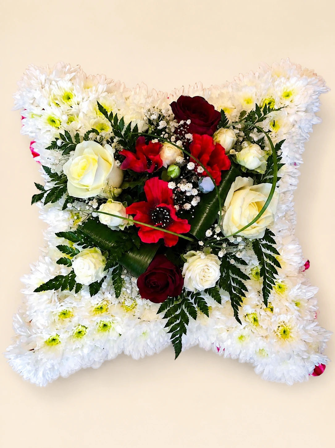 White floral funeral cushion with a central corsage of red and cream roses and fern foliage