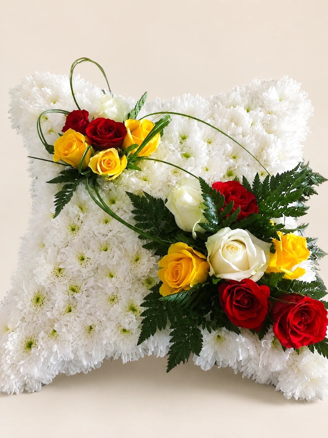 White floral funeral pillow with red, yellow and cream rose clusters and curved decorative grasses