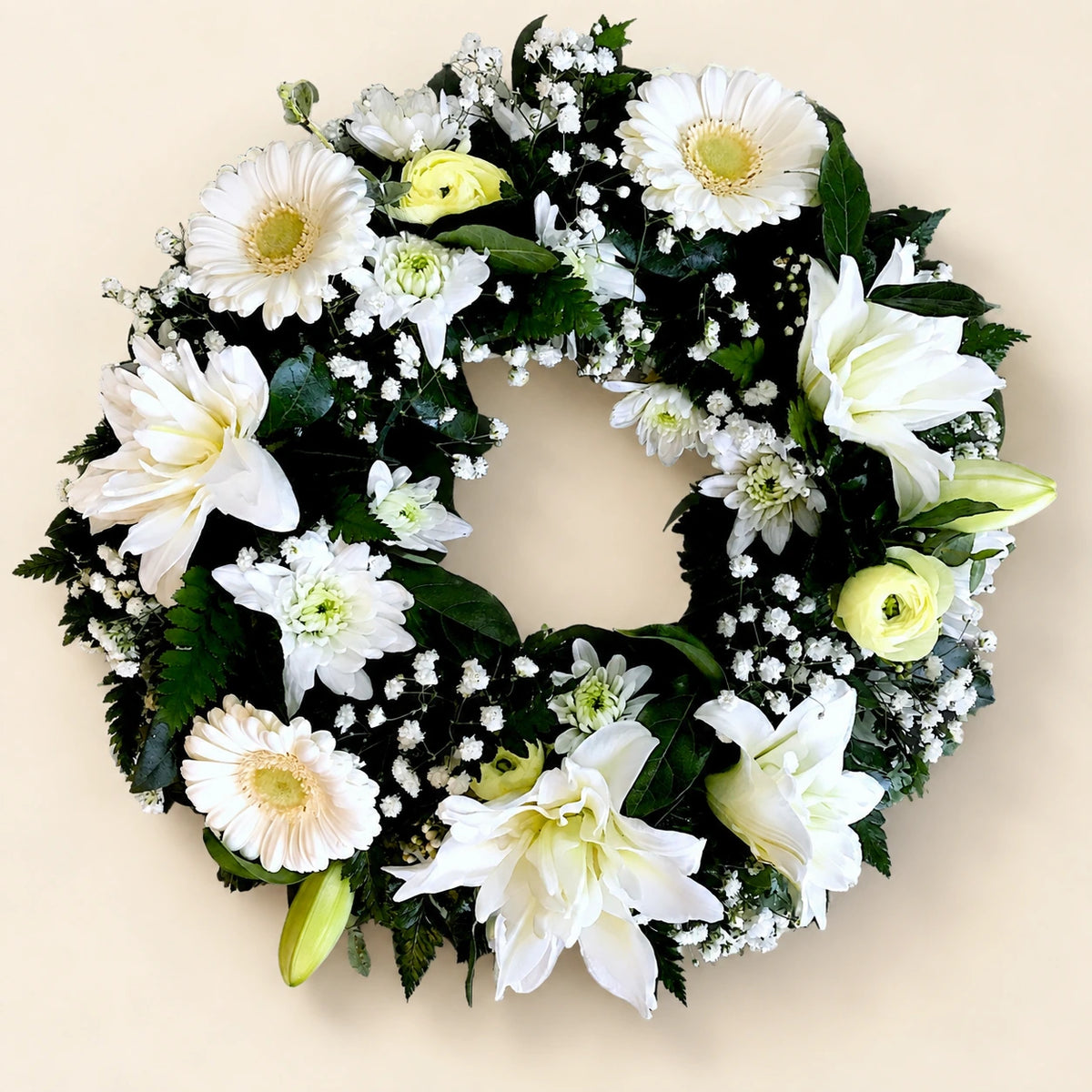 White funeral wreath with lilies, gerberas, small white flowers and dark green foliage